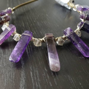 May include: A gold headband with amethyst crystals wrapped in wire. The crystals are long and pointed, and they hang down from the headband.