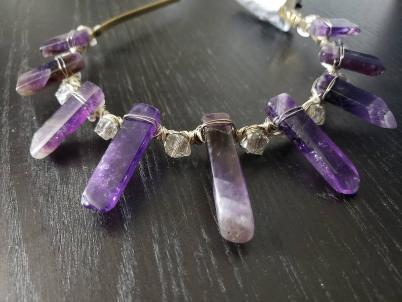 May include: A gold headband with amethyst crystals wrapped in wire. The crystals are long and pointed, and they hang down from the headband.