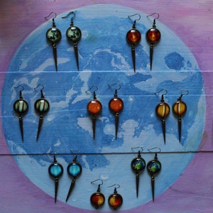 May include: A set of 10 pairs of earrings with different colored glass globes. The earrings are displayed on a blue and purple background.