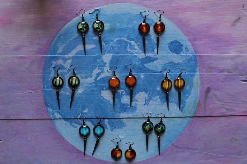 May include: A set of 10 pairs of earrings with different colored glass globes. The earrings are displayed on a blue and purple background.