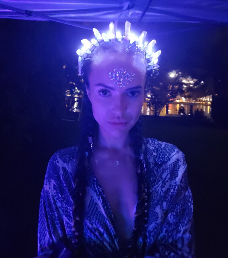 May include: A woman wearing a white crystal crown with lights, a silver nose ring, and a blue and white patterned shirt.