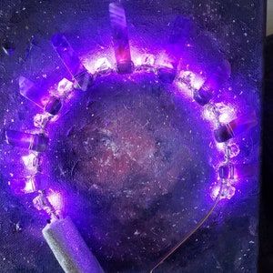 May include: A purple crystal headband with embedded LED lights, creating a glowing effect. The headband is made of metal and has a silver finish.