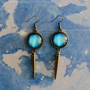 May include: A pair of dangle earrings with a blue and white galaxy design. The earrings have a bronze finish and a pointed spike hanging from the bottom.