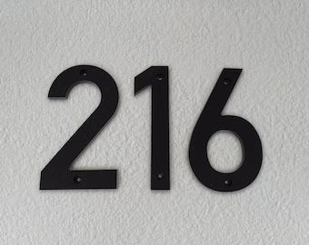 May include: Black metal house numbers 216, mounted on a white wall.