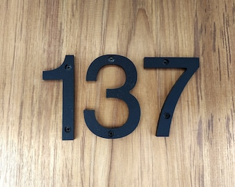 May include: Black metal house numbers 137 mounted on a wooden surface.
