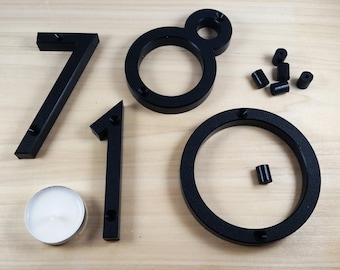 May include: Black plastic house numbers 7, 1, 0 and 8 with mounting screws. The numbers are on a light wood surface.