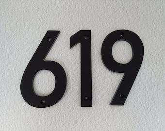 May include: Three individual house numbers forming the sequence 619, crafted in a matte black finish. Each numeral features a clean, sans-serif typeface with visible circular mounting holes at the top and bottom for secure installation on a wall.