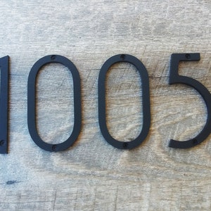 May include: Black metal house numbers, 1005, mounted on a wood surface.