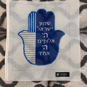 May include: A blue and white hand-shaped canvas with Hebrew text that reads "May you be protected from the evil eye".