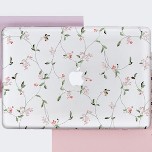 May include: A white laptop with a floral design on the lid. The design features pink flowers and green leaves on a white background. The laptop is sitting on a pink surface.