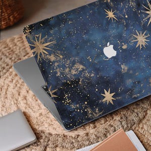 Op de afbeelding: Een laptop met een blauw en gouden galaxy-ontwerp. Het ontwerp bevat gouden sterren en een subtiel gouden glitter-effect.