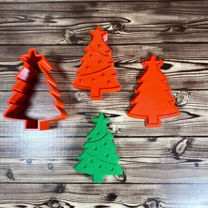 May include: Four Christmas tree cookie cutters, three are red and one is green. The red cutters have a star on top and the green cutter has a star on top and a swirl design.