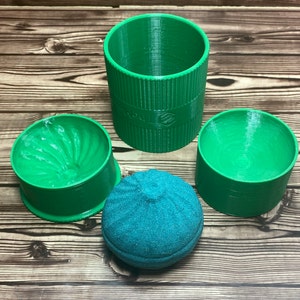 May include: A set of three green plastic containers with a teal-colored sponge ball. The containers have a smooth, rounded exterior and a textured interior.