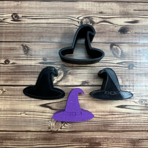 May include: Three black witch hat cookie cutters and one purple witch hat cookie cutter on a wooden surface.