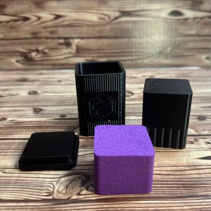 May include: Four small black boxes with a textured surface and a purple box with a textured surface. The black boxes have a logo on the front.