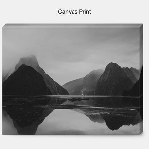 May include: Black and white photograph of a mountain range reflected in a still body of water. The mountains are covered in fog and the water is calm and serene.