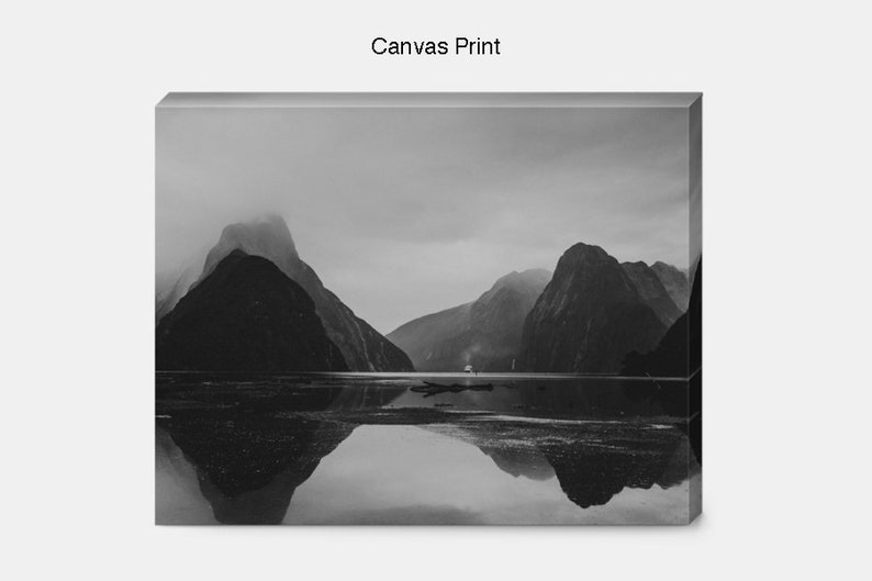 May include: Black and white photograph of a mountain range reflected in a still body of water. The mountains are covered in fog and the water is calm and serene.