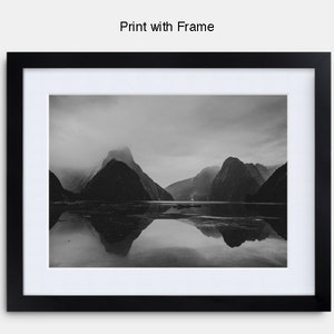 May include: A black and white photograph of a mountain range reflected in a still body of water. The mountains are shrouded in mist and the water is calm and serene.