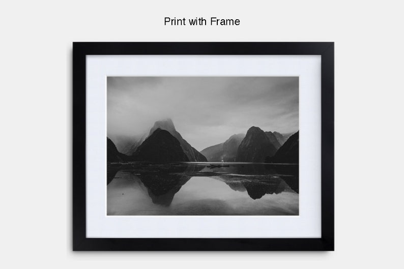 May include: A black and white photograph of a mountain range reflected in a still body of water. The mountains are shrouded in mist and the water is calm and serene.