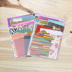 May include: Two clear plastic sleeves containing an assortment of decorative paper scraps and cardstock pieces. The collection features various textures, patterns, and colours, including floral prints, geometric designs, solid colours, and a striped envelope.