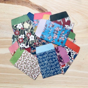 May include: A collection of rectangular paper envelopes featuring various patterns including cherry blossoms, floral motifs, and geometric designs in colours such as blue, red, green, pink, and black, arranged in a circular overlapping fan formation.
