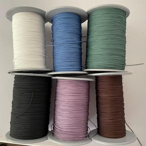 May include: Six spools of thread in different colours: white, blue, green, black, pink, and brown. The spools are all the same size and are arranged in two rows of three.