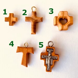 May include: Five different wooden cross pendants, each with a unique design. The crosses are made of light brown wood and have a natural finish. The pendants are numbered 1 through 5.