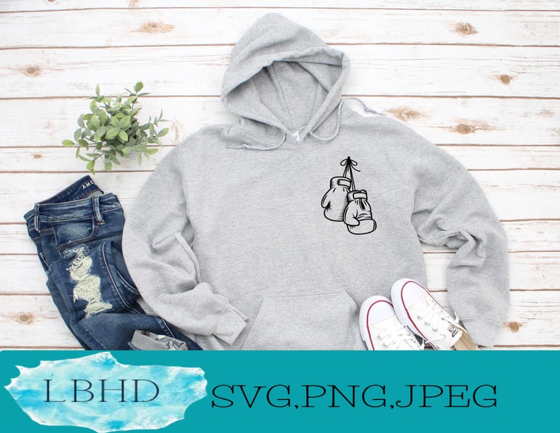 May include: A gray hoodie with a black outline of boxing gloves hanging from a string. The hoodie is on a white wooden background.