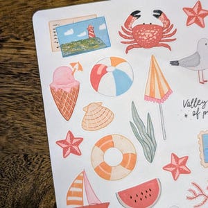 Może przedstawiać: Kolekcja kolorowych naklejek o tematyce letniej z r&oacute;żnymi ilustracjami. Naklejki zawierają kraba, lody, piłkę plażową, muszlę, żagl&oacute;wkę, plaster arbuza i aparat fotograficzny. Naklejki są na białym tle.