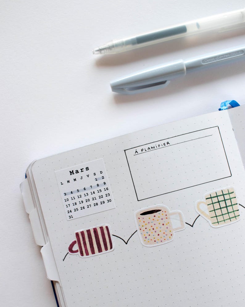 May include: A white planner with a calendar for March, a section labeled "A PLANIFIER", and a row of colorful coffee cup stickers.
