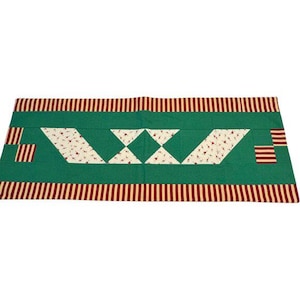 May include: A rectangular quilt with a green central panel featuring white and red floral patterned triangles and diamonds. The quilt is bordered by red and white striped fabric.