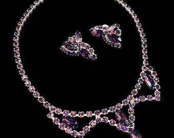 May include: A vintage jewelry set featuring a necklace and matching earrings. The necklace and earrings are adorned with purple gemstones set in a gold-tone metal. The necklace has a bib design with a central pendant.