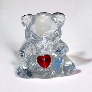 May include: A clear glass teddy bear figurine holding a red heart in its paws.