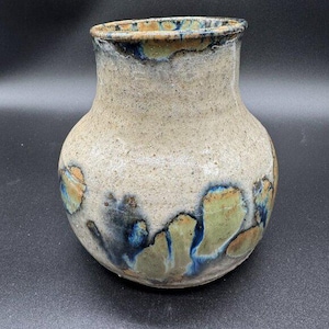 May include: A handcrafted ceramic vase with a speckled beige body and a rounded shape. The vase features blue, green, and orange accents around the base and rim. The vase is approximately 18 cm tall.