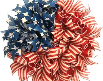 May include: A round wreath featuring a patriotic design. The left side is blue with white stars, and the right side has red and white striped ribbons. The wreath is made of layered ribbons and is suitable for door or wall decor.