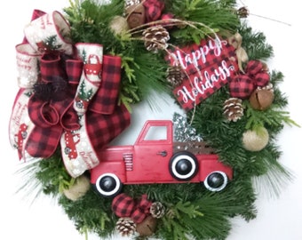 May include: A festive Christmas wreath with a red truck carrying a tree. The wreath features pine needles, pine cones, and red and black plaid accents. A red and white ribbon with the words "Special Delivery" is also included. The sign says "Happy Holidays".