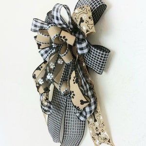 May include: A black and white checkered ribbon, a brown ribbon with white paw prints, and a brown ribbon with white paw prints and bone designs are tied together in a bow.
