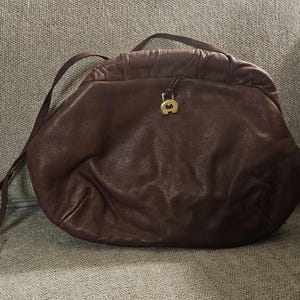 May include: A brown leather handbag with a single strap and a gold clasp. The bag has a soft, slouchy look.