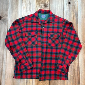 May include: A red, green, and blue plaid shirt with a button-down front and two chest pockets. The shirt features a classic collar and long sleeves. The fabric looks like a thick, warm material, suitable for cooler weather.