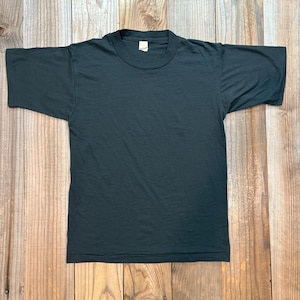 May include: A dark grey, short-sleeved t-shirt with a crew neck. The shirt is displayed flat, highlighting its plain design and solid colour. The fabric looks soft and slightly worn, possibly indicating a vintage or well-used item.
