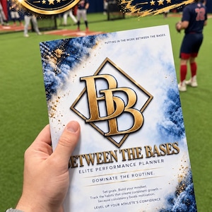 May include: A white planner cover with blue and gold smoke-like accents, featuring a large gold BB logo inside a diamond shape. Text reads: BETWEEN THE BASES, ELITE PERFORMANCE PLANNER, DOMINATE THE ROUTINE, and Set goals. Build your mindset.
