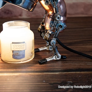 May include: A silver and copper steampunk-style lamp with a black cord, illuminating a white Yankee Candle jar with the text "Wedding Day".