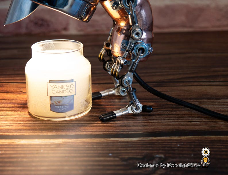 May include: A silver and copper steampunk-style lamp with a black cord, illuminating a white Yankee Candle jar with the text "Wedding Day".