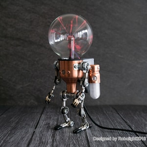 May include: Steampunk-style robot lamp with a clear glass head containing red plasma. The body is copper-colored, with articulated metal limbs and a small white light fixture on the side. The lamp is designed by Robolight2018.