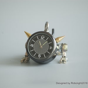May include: A black clock with gold accents and a silver metal body. The clock has a black face with white numbers and hands. The clock is attached to a silver metal chain.