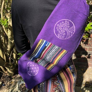 May include: A deep purple yoga mat bag with a tree of life and flower of life design. The bag has a colorful woven pocket and is slung over the shoulder. The bag is made of a soft fabric.