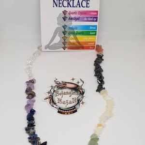 May include: A colorful chakra necklace with a variety of gemstones, including quartz crystal, amethyst, and green quartz. The necklace is displayed with a card that has the text "CHAKRA NECKLACE". A sticker with the text "Bojangles Bazar" is also visible.