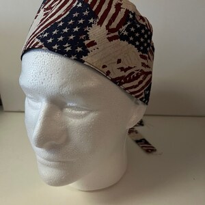 May include: A surgical scrub hat with a red, white, and blue American flag pattern. The hat has a tie at the back.