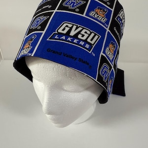 Peut inclure: Un bonnet de chirurgien à motifs bleus, noirs et blancs avec le texte "GVSU LAKERS" et le logo Grand Valley State. Le bonnet est en tissu et est conçu pour être porté sur la tête.