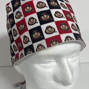 Peut inclure: Un bonnet de travail blanc, rouge et noir à motif avec un personnage de dessin animé répété sur tout le design. Le personnage porte un chapeau rouge et blanc et a un visage brun. Le chapeau a une bordure blanche autour du bord.